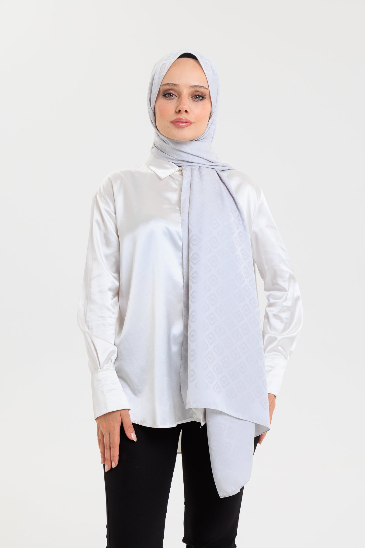 Woman wearing a light gray hijab and white blouse on a white background