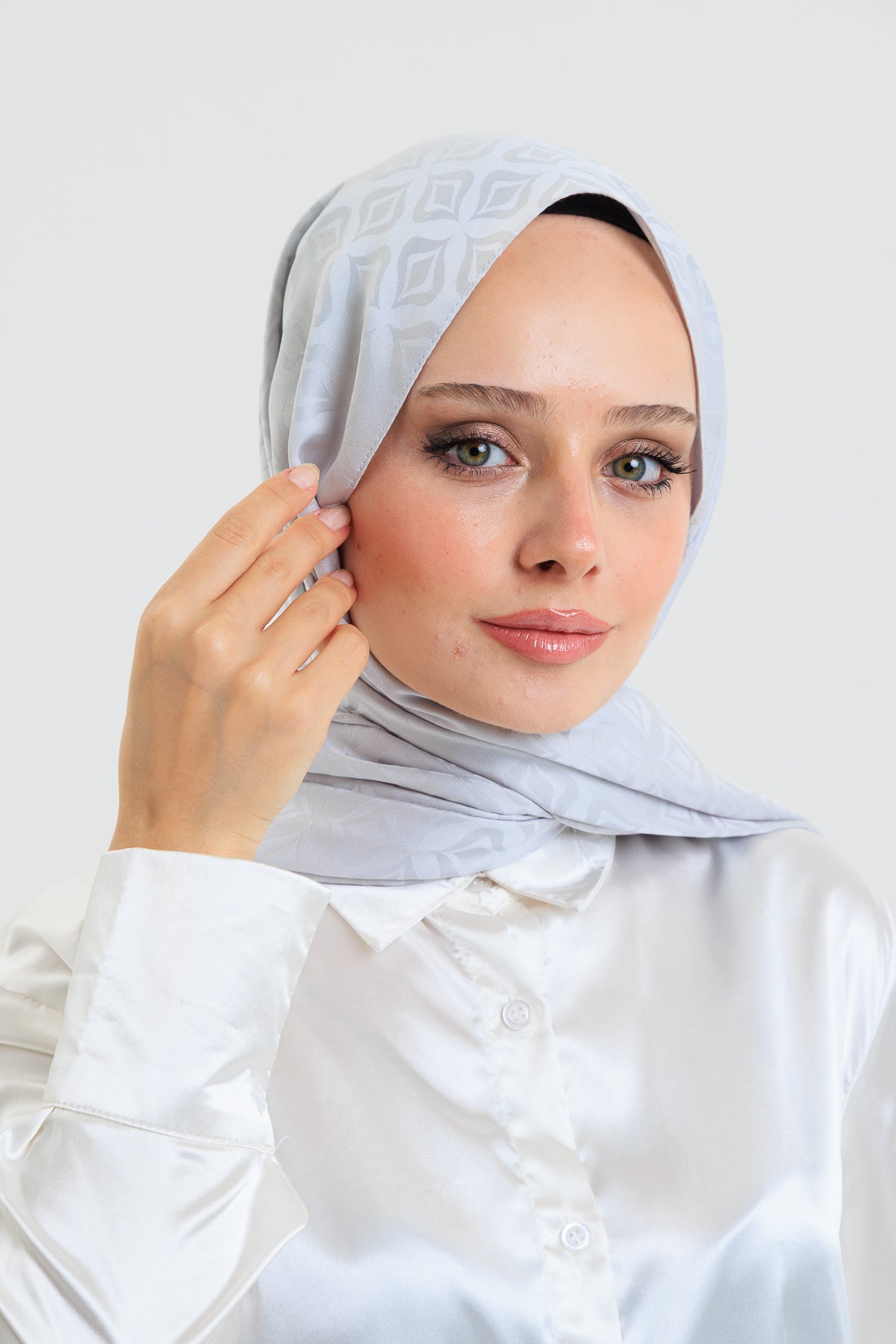Woman wearing a light gray hijab against a white background