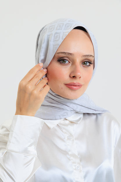 Woman wearing a light gray hijab against a white background