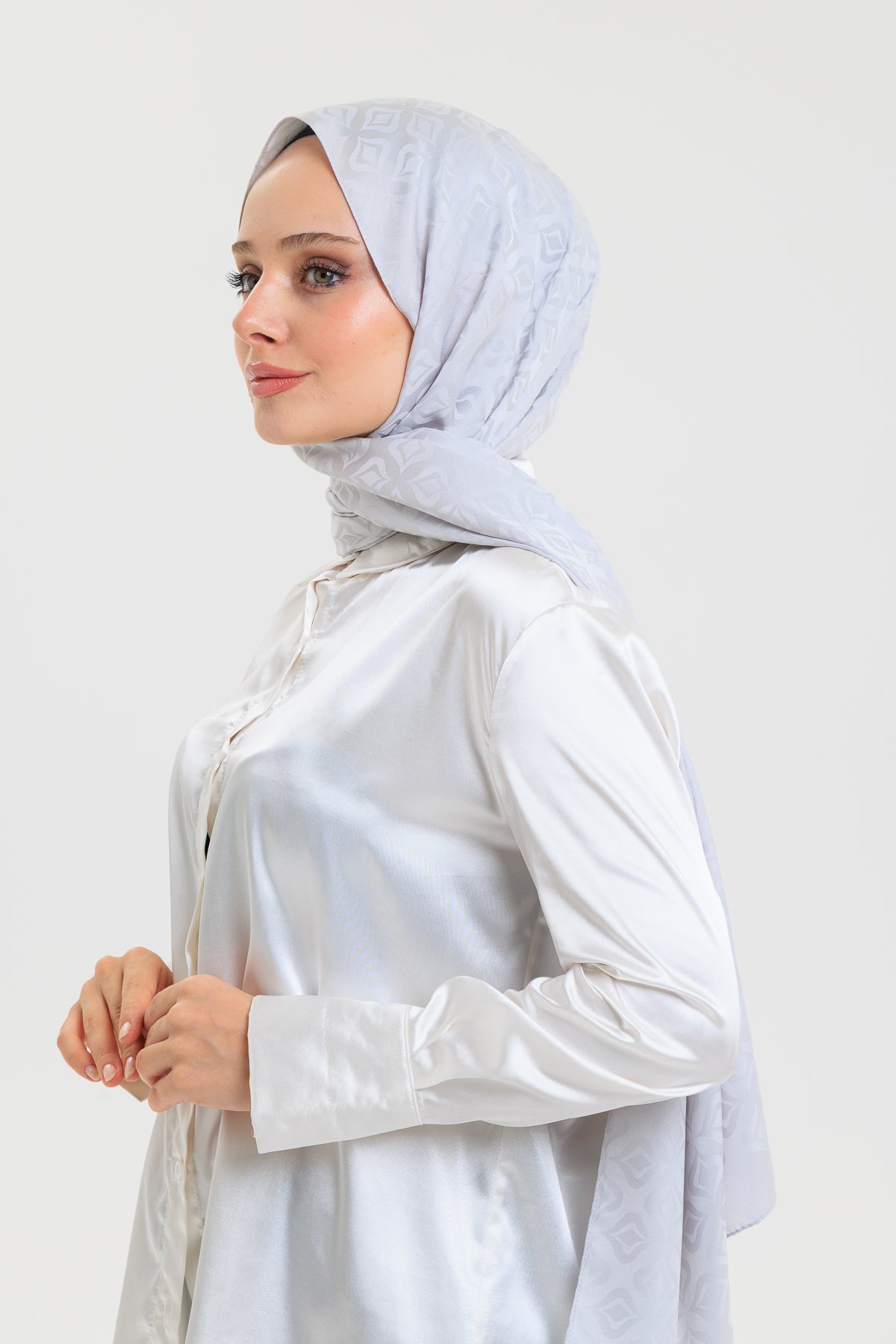 Woman wearing a light blue hijab and white shirt against a plain background