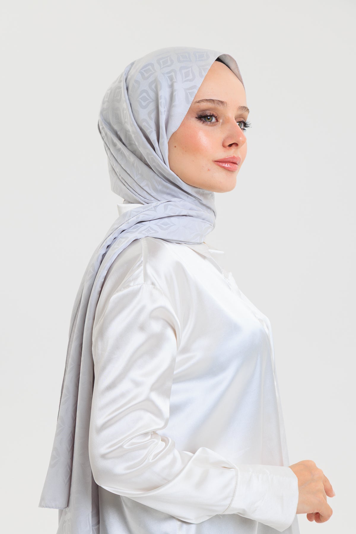Woman wearing a light gray hijab with floral patterns on a white background