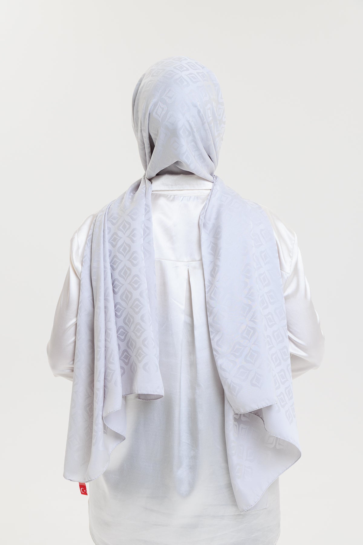 Person wearing a light gray hijab and outfit on a plain background