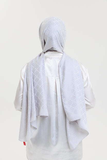 Person wearing a light gray hijab and outfit on a plain background