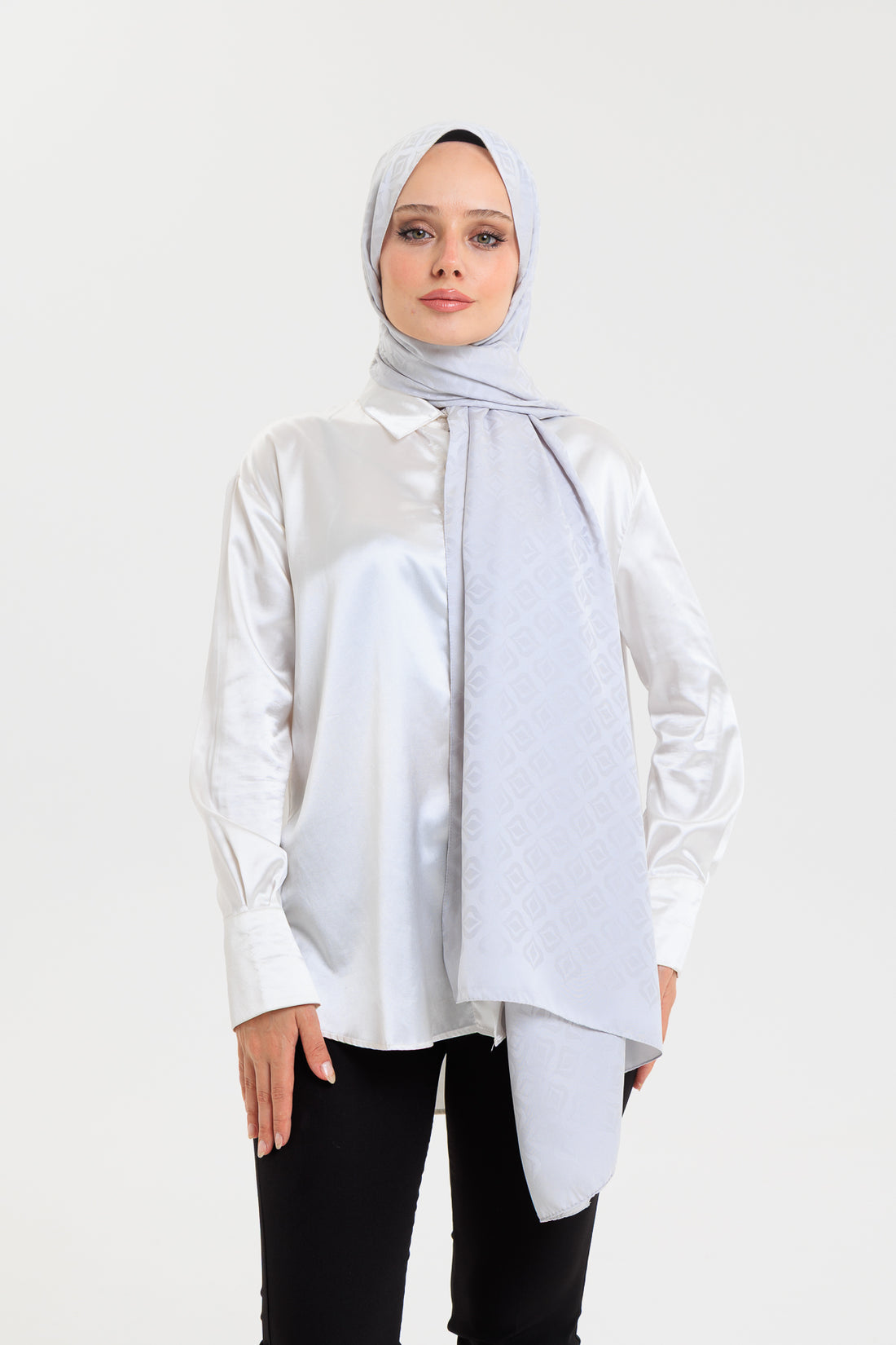 Woman wearing a light gray hijab and white blouse on a white background