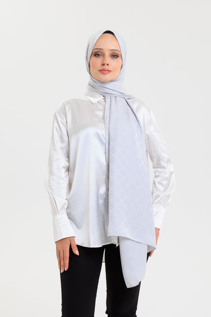 Woman wearing a light gray hijab and white blouse on a white background