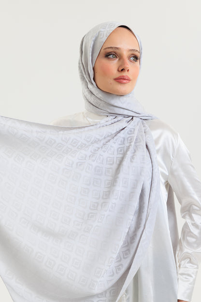 Woman wearing a light gray hijab and white outfit against a white background